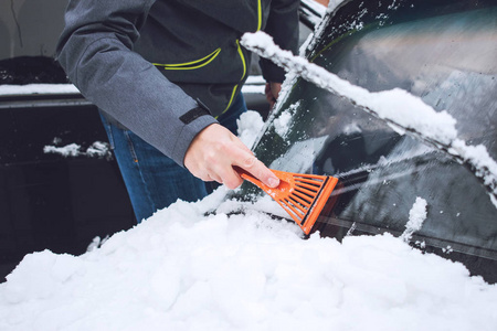 在降雪期间，人们用刷子和刮刀工具从雪和冰中清洗汽车。 冬季紧急情况。 天气相关的车辆紧急情况。 覆盖着雪的汽车