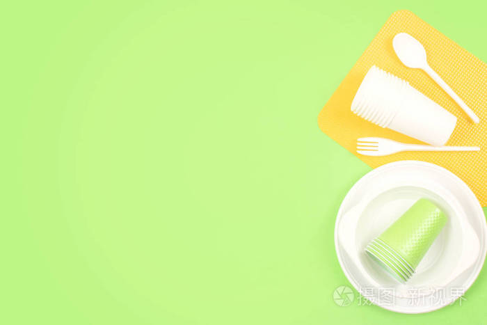 绿色背景上的彩色明亮塑料一次性餐具.