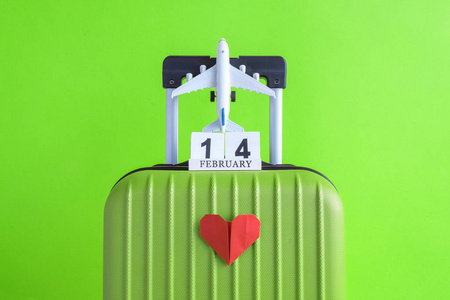 手提箱与2月14日木制日历和飞机模型玩具折纸红心绿色背景最小创意旅行概念。