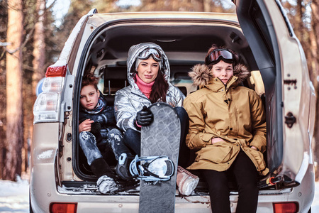一个漂亮的女人和她的儿子们穿着温暖的衣服坐在汽车后备箱上