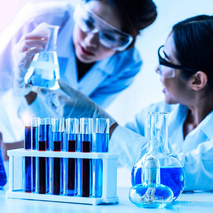 一组科学家穿着实验室外套在实验室工作,同时检查试管和科学仪器中的