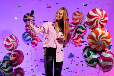 戴着智能手机耳机的女孩在紫色背景的糖果色气球上唱一首歌