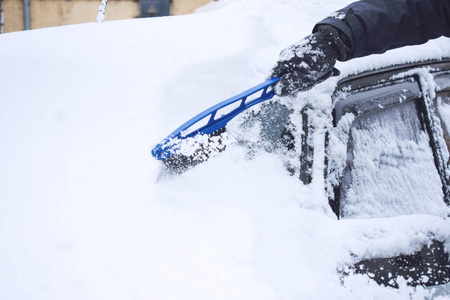 在降雪期间，人们用刷子和刮刀工具从雪和冰中清洗汽车。 冬季紧急情况。 天气相关的车辆紧急情况。 覆盖着雪的汽车