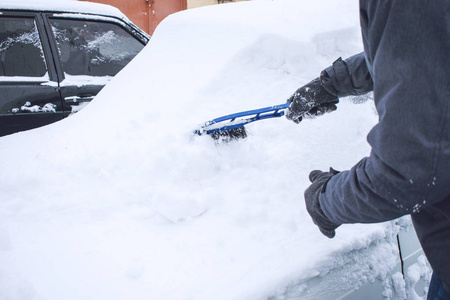 在降雪期间，人们用刷子和刮刀工具从雪和冰中清洗汽车。 冬季紧急情况。 天气相关的车辆紧急情况。 覆盖着雪的汽车