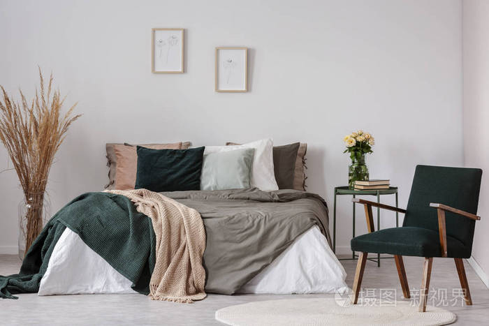 木制扶手椅旁边的床和桌子与花在白色简单的卧室内部真实照片