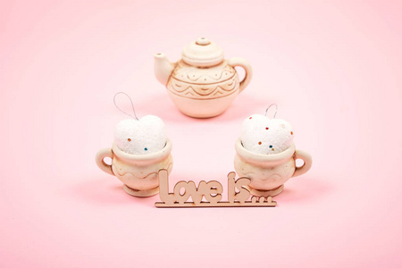 情人节粘贴最小背景。 两个粘土杯，心和茶壶在粉红色的背景。 婚礼优雅的爱情浪漫概念。 选择性聚焦。