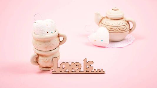 情人节粘贴最小背景。 两个粘土杯，心和茶壶在粉红色的背景。 婚礼优雅的爱情浪漫概念。 选择性聚焦。