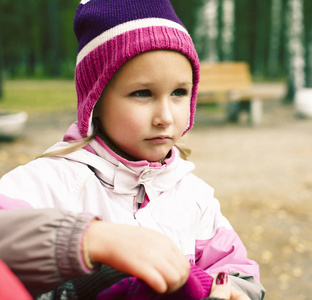 小女孩在帽子上打扮手套与母亲帮助在公园外