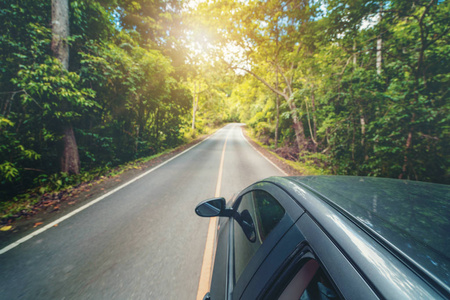 夏季在森林公路上行驶的黑色汽车的侧视图。 旅行和探索概念。