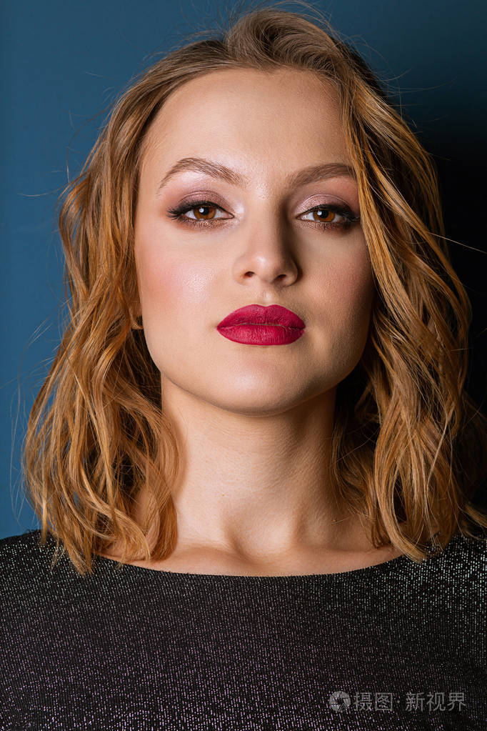 一幅美丽的金发女子的特写肖像她的妆容鲜艳留着波浪发摆在工作室里