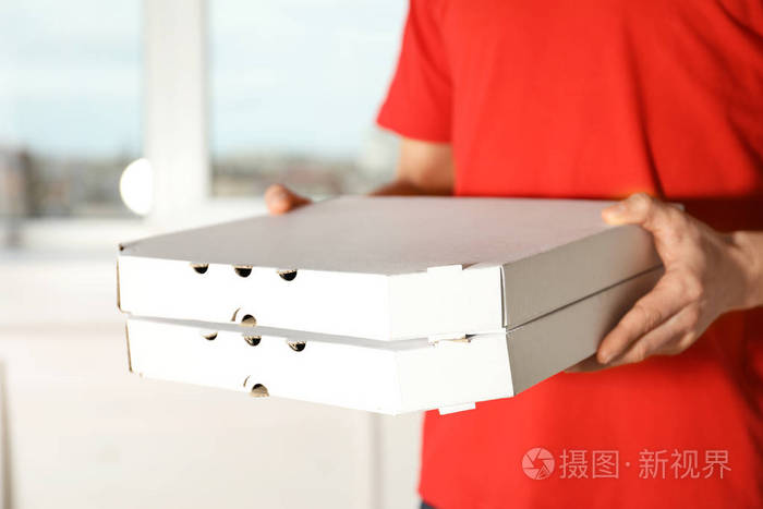年轻人带着披萨盒在室内特写。 食物供应服务
