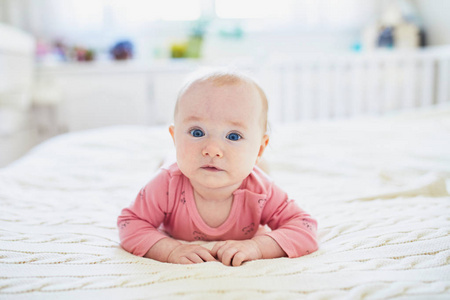 可爱的女婴躺在床上肚子上。 快乐健康的孩子练习爬行。 在阳光充足的托儿所做肚子的婴儿