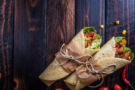 传统的墨西哥玉米饼包装，蔬菜和烤鸡肉在深色木桌上