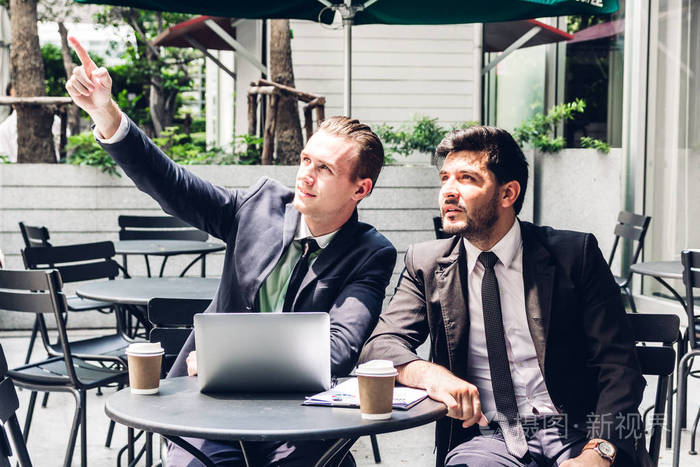 两个穿黑色西装的商人同事在咖啡馆里交谈和工作,一起讨论一些事情.