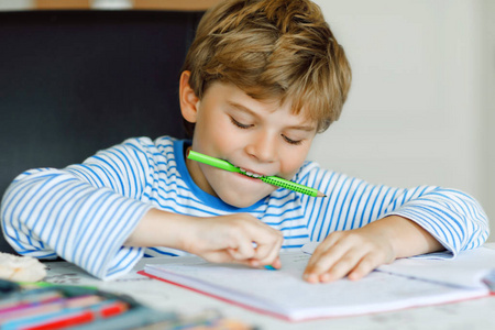 可爱健康快乐学校的孩子的肖像在家做家庭作业。小孩子用五颜六色的铅笔写字, 在室内。小学和教育。学习写信和数字的孩子