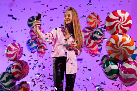 戴着智能手机耳机的女孩在紫色背景的糖果色气球上唱一首歌