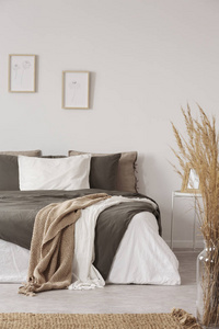 毯子在床上，枕头在白色的最小卧室内部，植物和海报。 真实照片