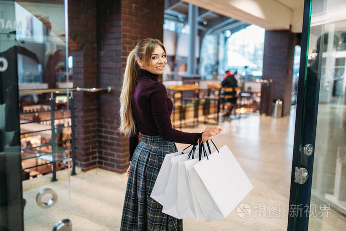 年轻的女人在商场里带着购物袋。 购物狂在服装店消费生活方式时尚有吸引力的女士购物