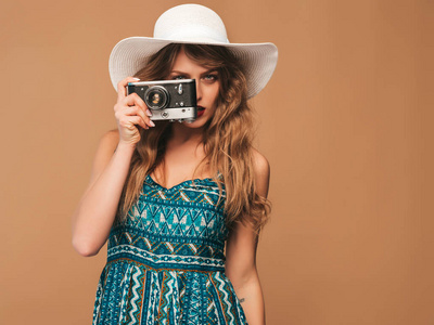 开朗微笑的年轻女子的肖像，带着灵感拍照，穿着夏季服装。 拿着复古相机的女孩。 戴帽子的金色背景模特