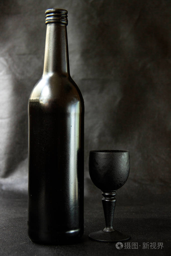 黑色皮革背景上带有黑色玻璃的黑色酒瓶