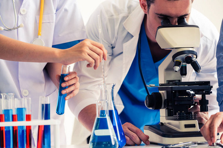 一组科学家穿着实验室外套在实验室工作,同时检查试管和科学仪器中的