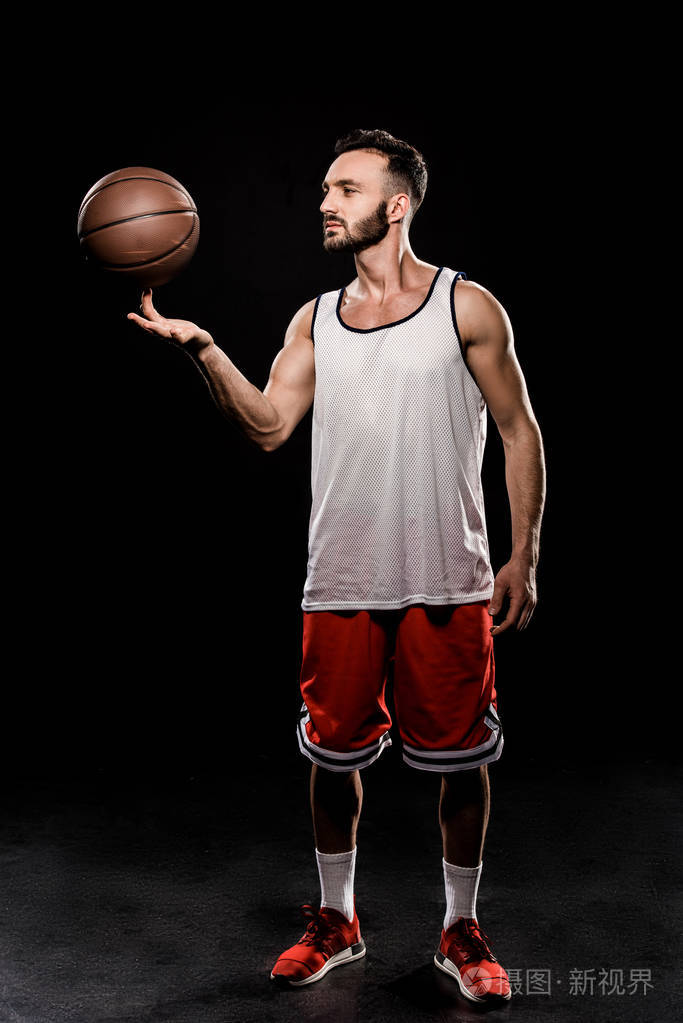 英俊的篮球运动员用手指在黑色背景上旋转球