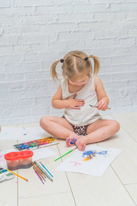 女孩用画笔和水彩颜料在一张纸和衣服上画画
