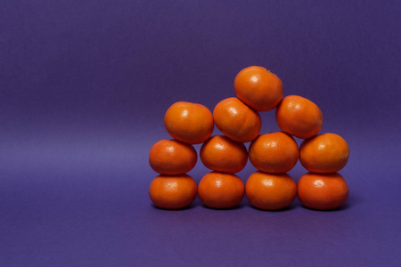 紫色背景上不对称的橘子堆叠。 复制空间的位置。