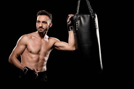 肌肉发达英俊的拳击手站在拳击袋附近，孤立于黑色