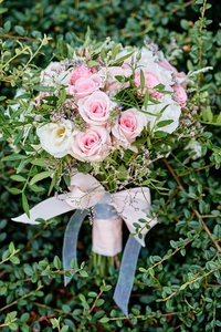 在绿叶背景上，用缎带蝴蝶结将粉红色玫瑰和绿色植物的小新娘花束合上，复制空间。婚礼概念
