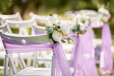 室外牌坊两侧各设白色木椅，配紫色布和白色牡丹花，复印空间..为宾客准备婚礼用的空椅子