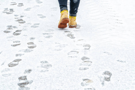 冬天穿黄色皮靴走路. 在一个人的脚上,沿着冰冷的雪路面行走的后景.