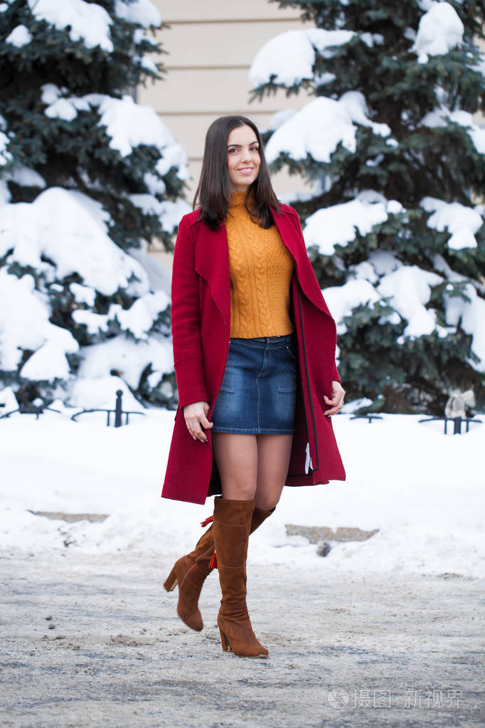 全身都是。 年轻漂亮的黑发女人穿着红色外套在冬季公园摆姿势。 模特穿着时尚温暖的衣服。