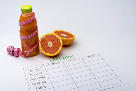饮食计划和一瓶葡萄柚汁与新鲜葡萄柚白色背景。 健康饮食的概念。