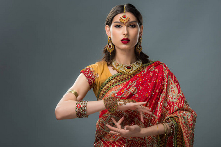 有吸引力的印度妇女在灰色隔离的传统服装中打手势
