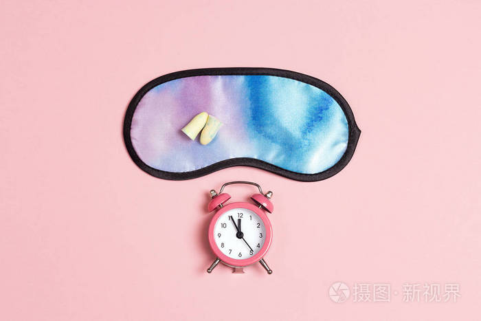 粉红色背景上的睡眠面罩耳塞和闹钟。 休息睡眠失眠放松旅行的概念。