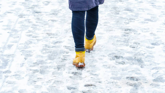 冬天穿黄色皮靴走路在一个女人的脚上沿着冰冷的雪路面行走冬天在结冰