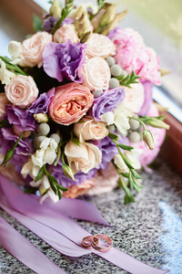 关闭新娘花束粉红色玫瑰牡丹紫色花朵和草药和两个金环在大理石窗台复制空间。 婚礼的概念。 选择性聚焦