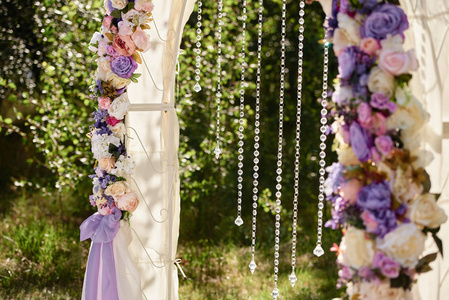 美丽的婚礼拱门装饰白色粉红色和紫色的花，水晶和布在花园户外复制空间。 婚礼安排。 仪式的地点。 花卉