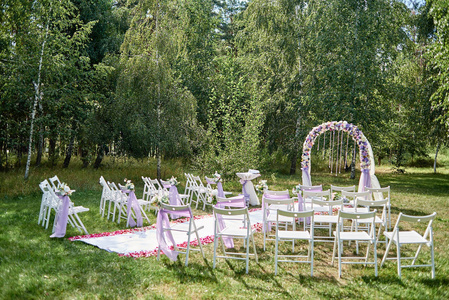 婚礼的地点。 婚礼拱门装饰布和鲜花和椅子在拱门的每一边的户外复制空间。 绿草上给客人的空木椅。 婚礼设置