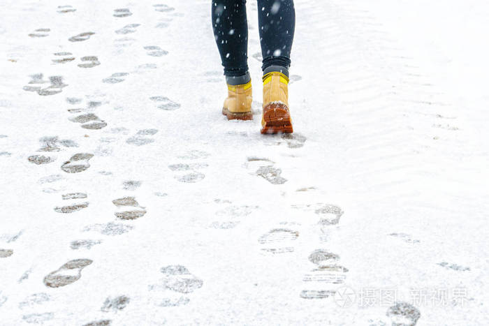 冬天穿黄色皮靴走路. 在一个人的脚上,沿着冰冷的雪路面行走的后景.