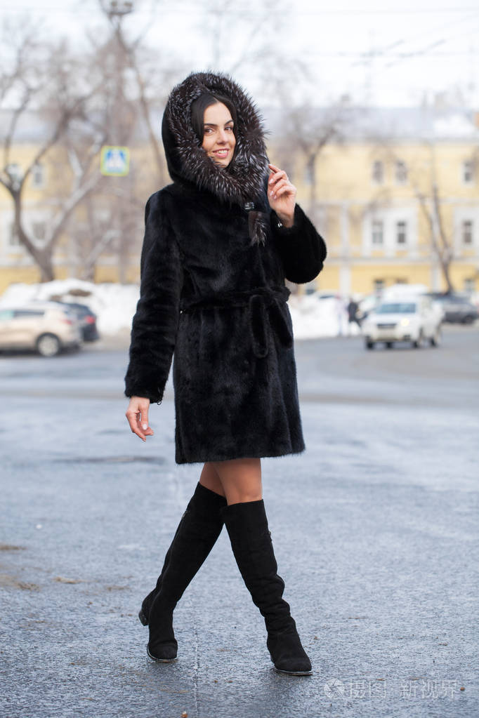 全身都是. 年轻漂亮的黑发女人穿着毛皮貂皮大衣在冬季公园摆姿势.