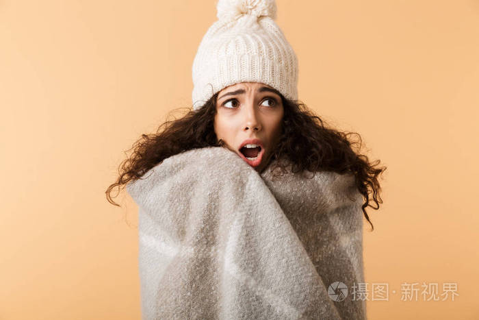 穿着冬巾的年轻女子被隔离在米色背景下瑟瑟发抖