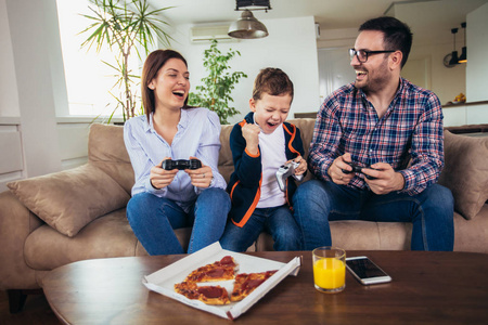 幸福的一家人坐在沙发上玩电子游戏，吃披萨