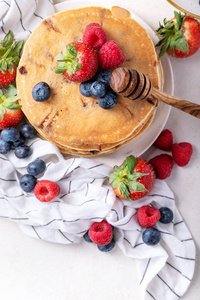 蓝莓薄煎饼与草莓，蓝莓，覆盆子，蜂蜜和枫糖浆在白色背景。 顶部视图