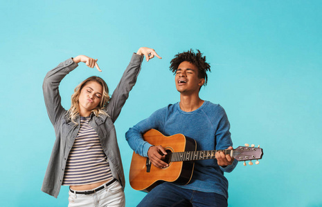快乐的年轻的多娘娘腔夫妇一起弹着蓝色背景下孤立的吉他