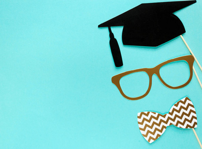 具有毕业摄影展位道具的创意背景帽子，毕业证，眼镜，嘴唇上亮蓝色纸背景..教育，学习理念..