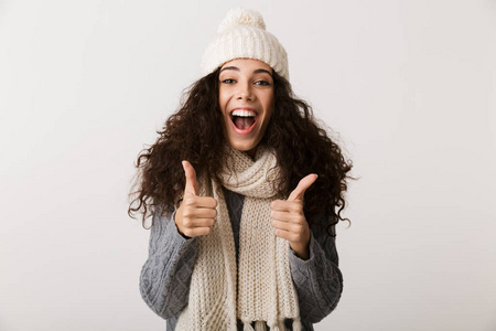 快乐的年轻女子穿着冬天的衣服，站在白色的背景上，竖起大拇指