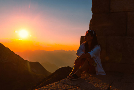 女人坐在边缘，在山上看到美丽的日落。暑假假期