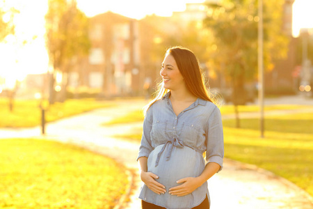 一位幸福的孕妇在日落时分在公园散步
